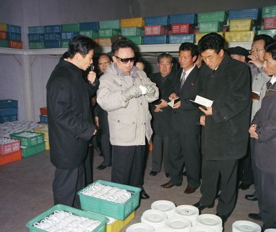 Ким Чен Ир осматривает посуду из твердого стекла. Ноябрь 2004 г.